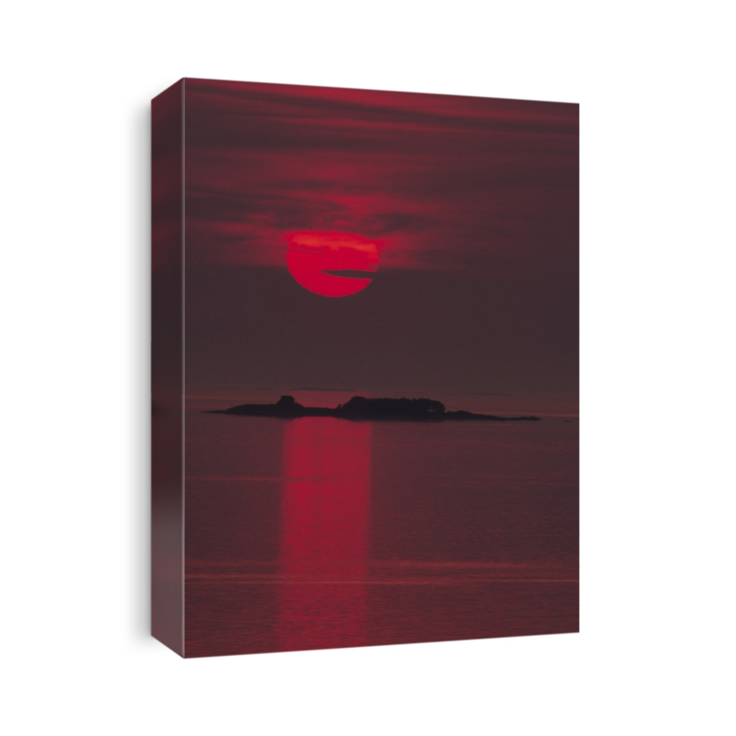 Sunset. A huge red sun sinks towards the sea's horizon, throwing a small island into silhouette.