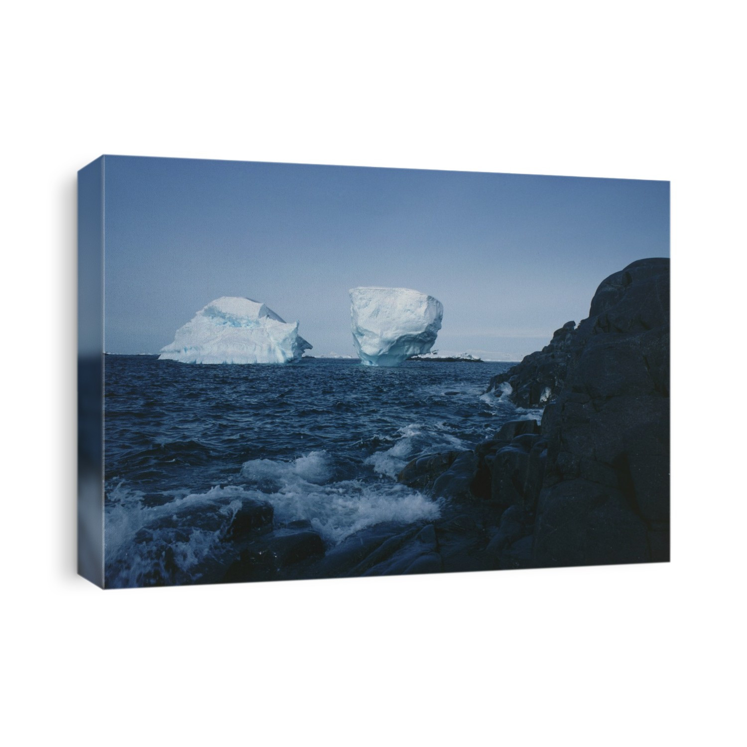 Icebergs off the Biscoe Islands, Antarctic peninsula. Of these bergs that have run aground, one has been so eroded by the action of the sea, that it overhangs on all sides. The top section will eventually break off and topple into the sea.