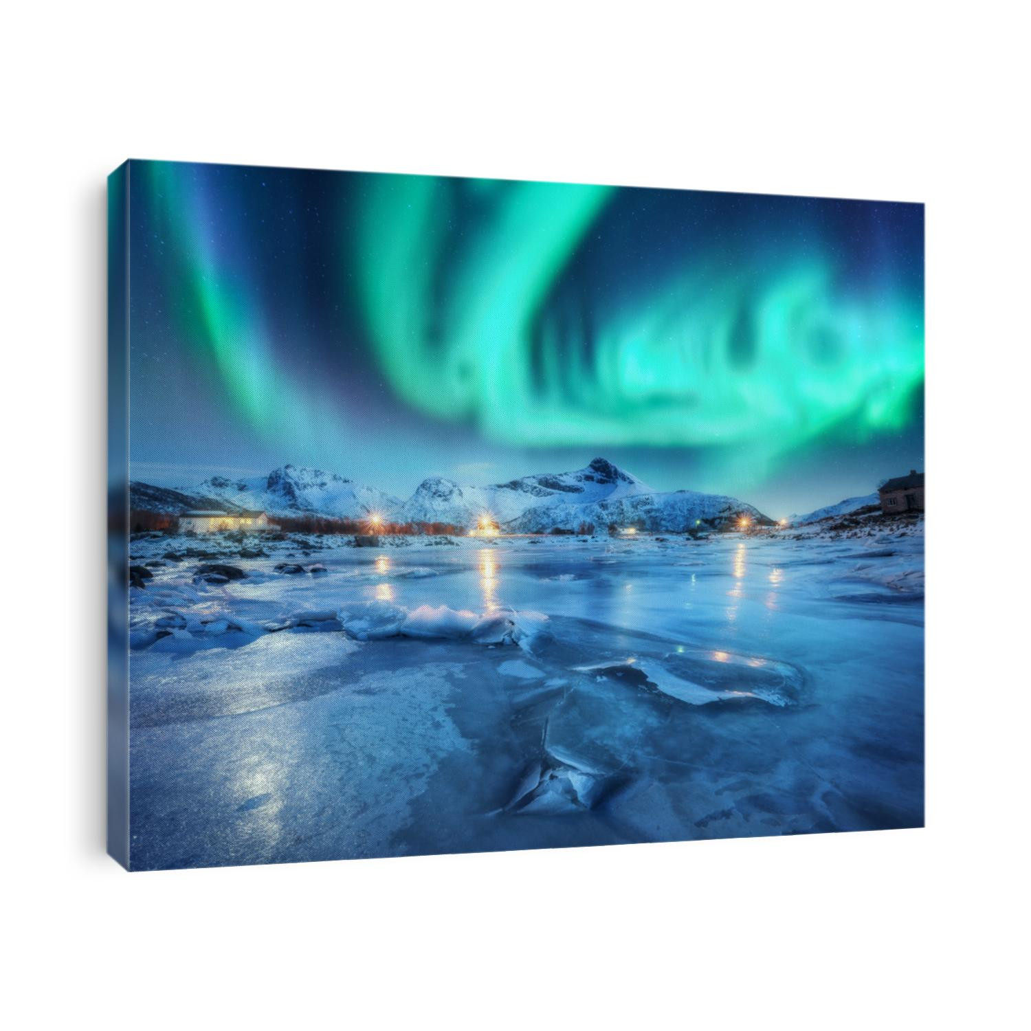 Northern lights above snowy mountains, frozen sea coast and houses in Lofoten islands, Norway. Aurora borealis and small village. Winter landscape with polar lights, rorbu, ice. Aurora over rocks