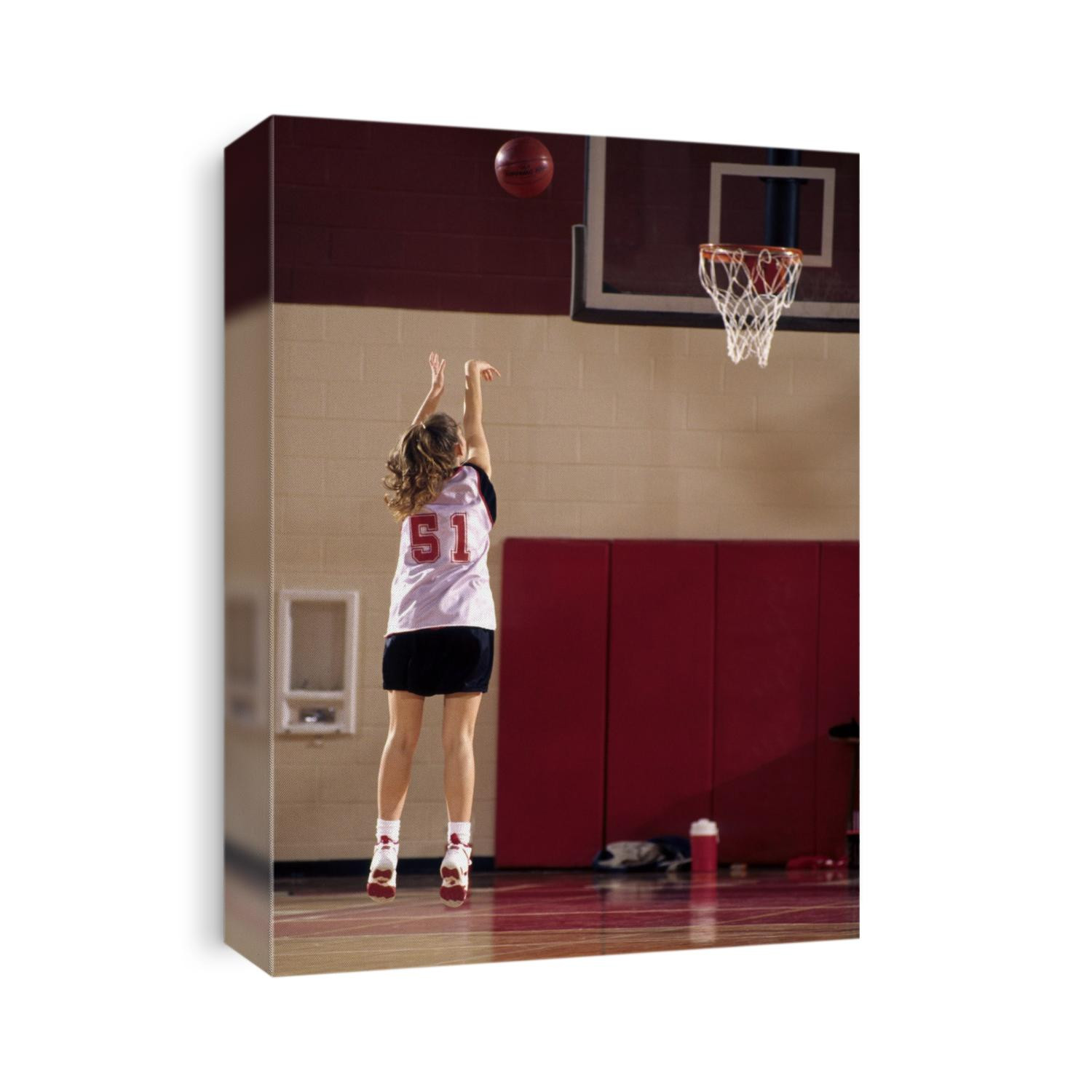 Teenage girl practicing basketball indoors,