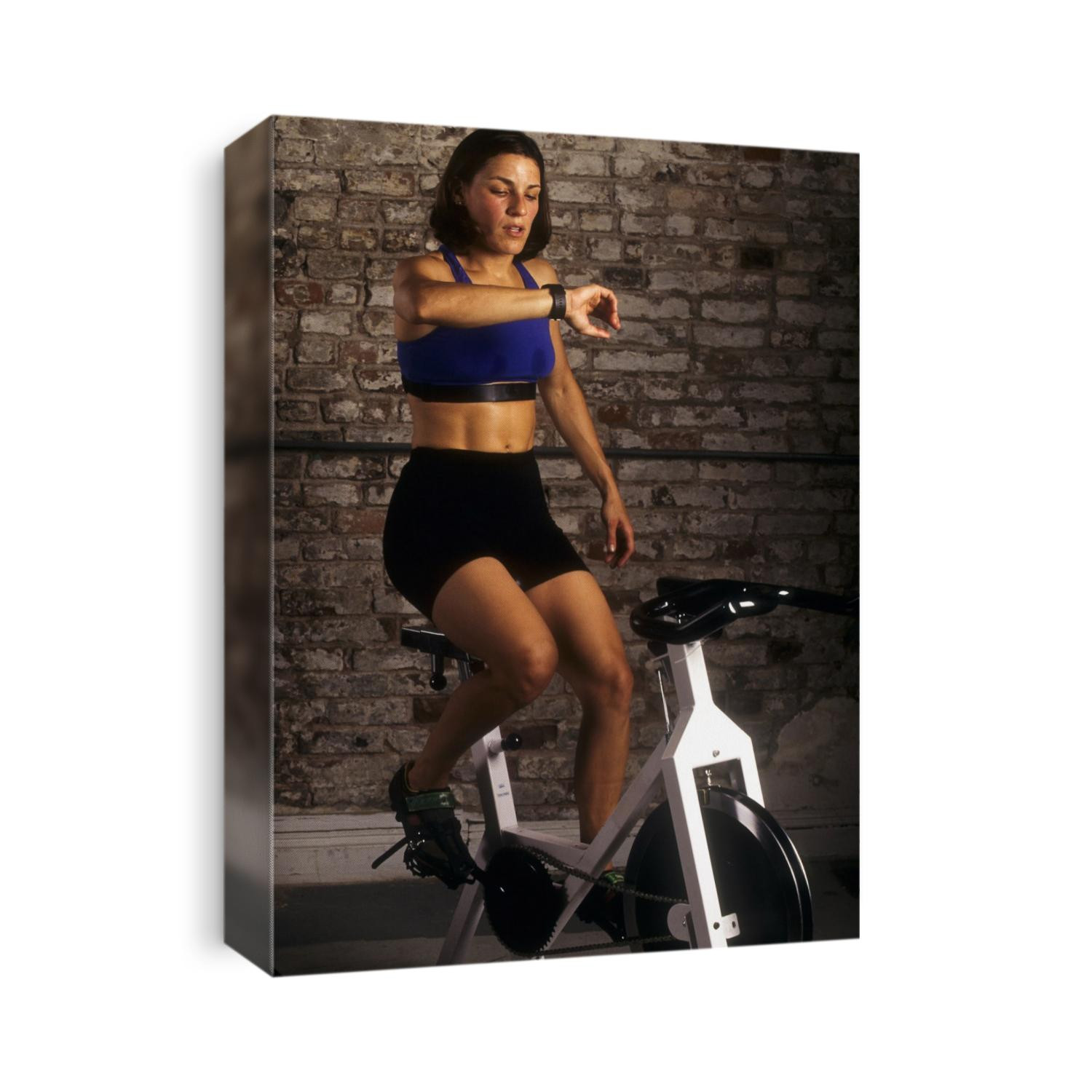 Young woman exercising on a stationary bike checking her heart rate.