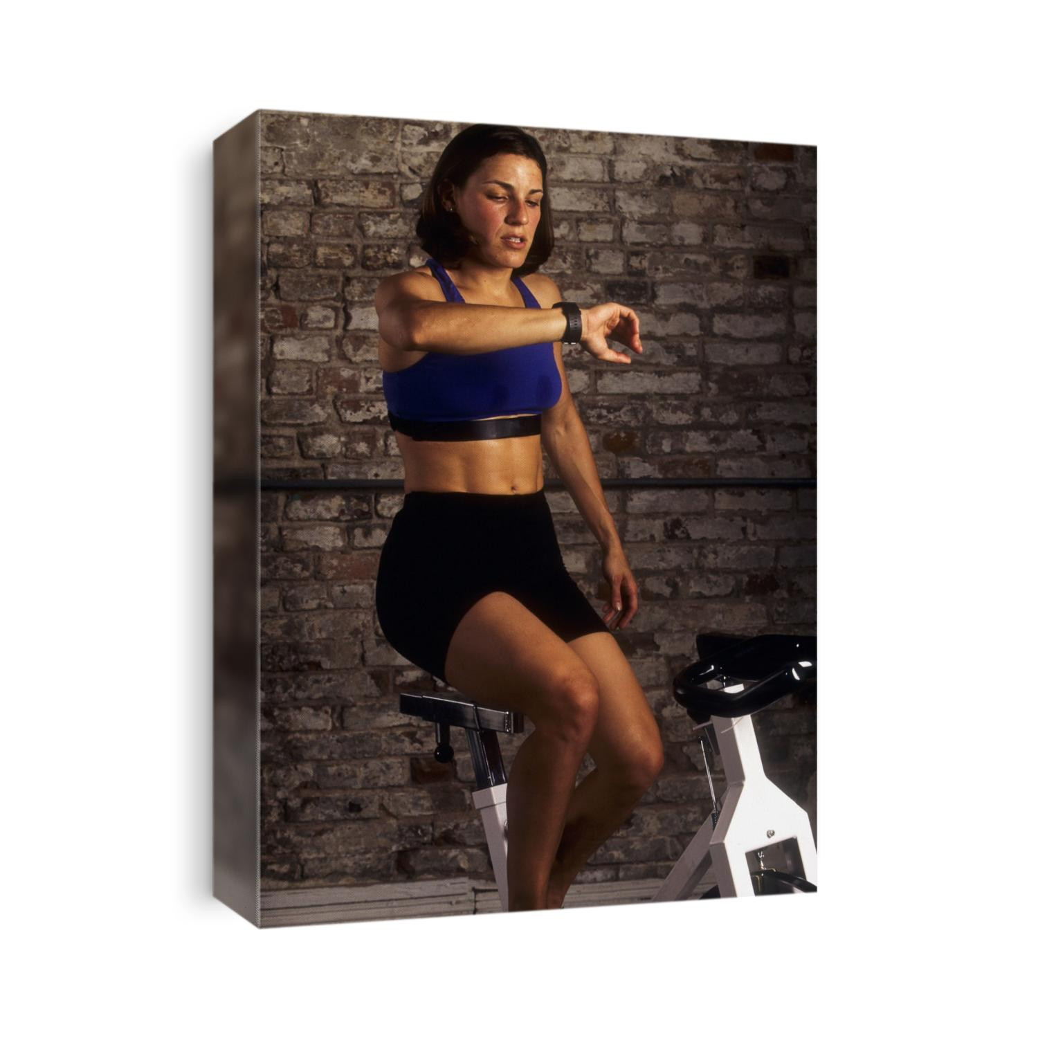Young woman exercising on a stationary bike checking her heart rate.