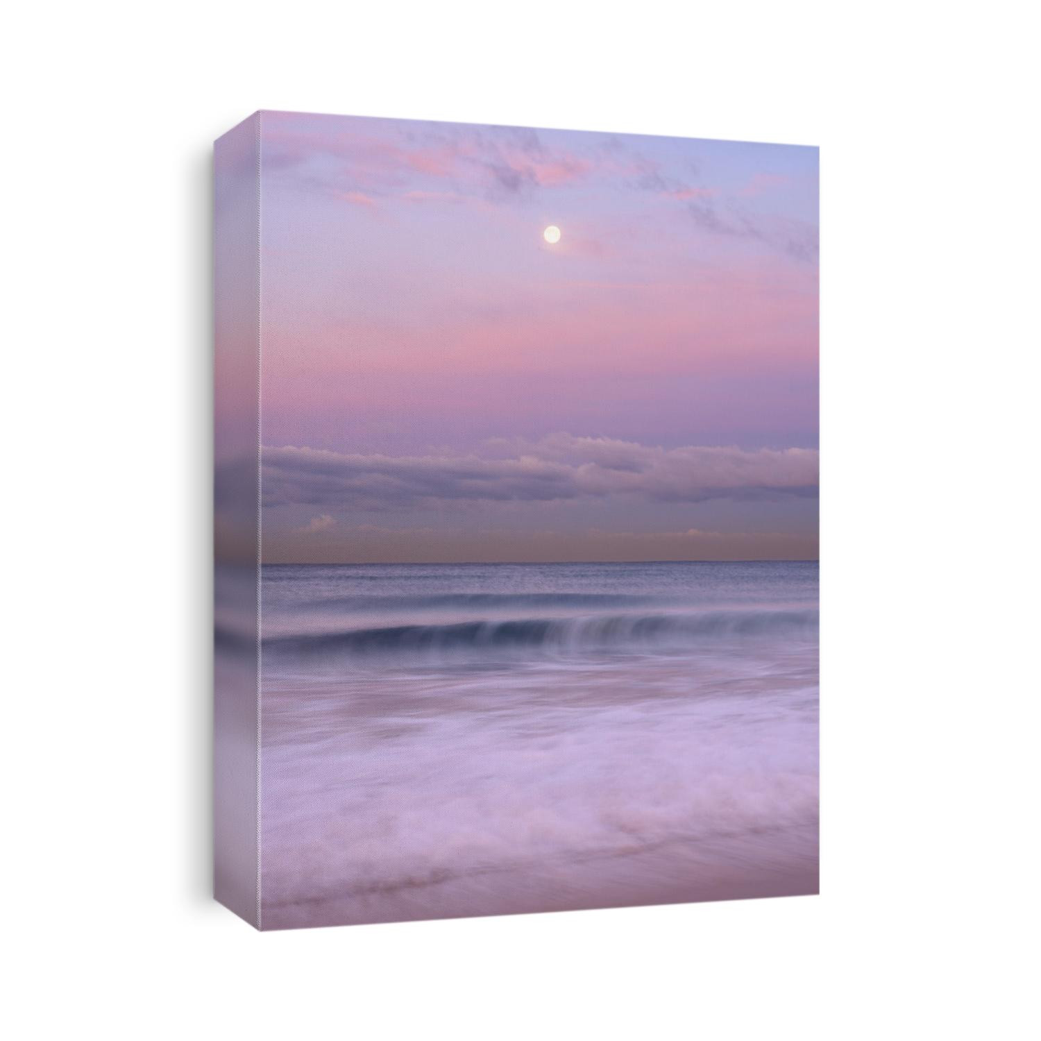 A full moon sets on a pastel morning set of waves in Manhattan Beach