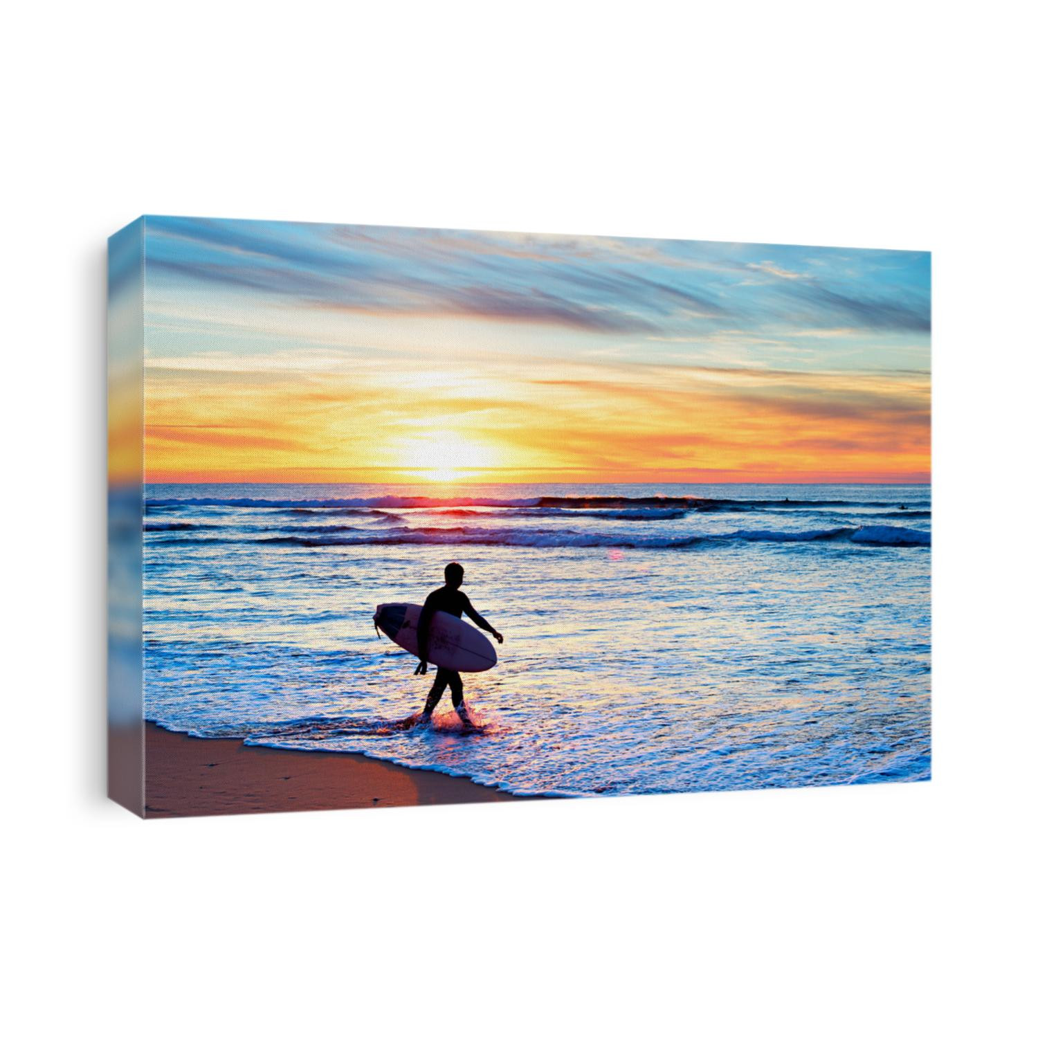 Surfer with surfboard walking on the beach at sunset
