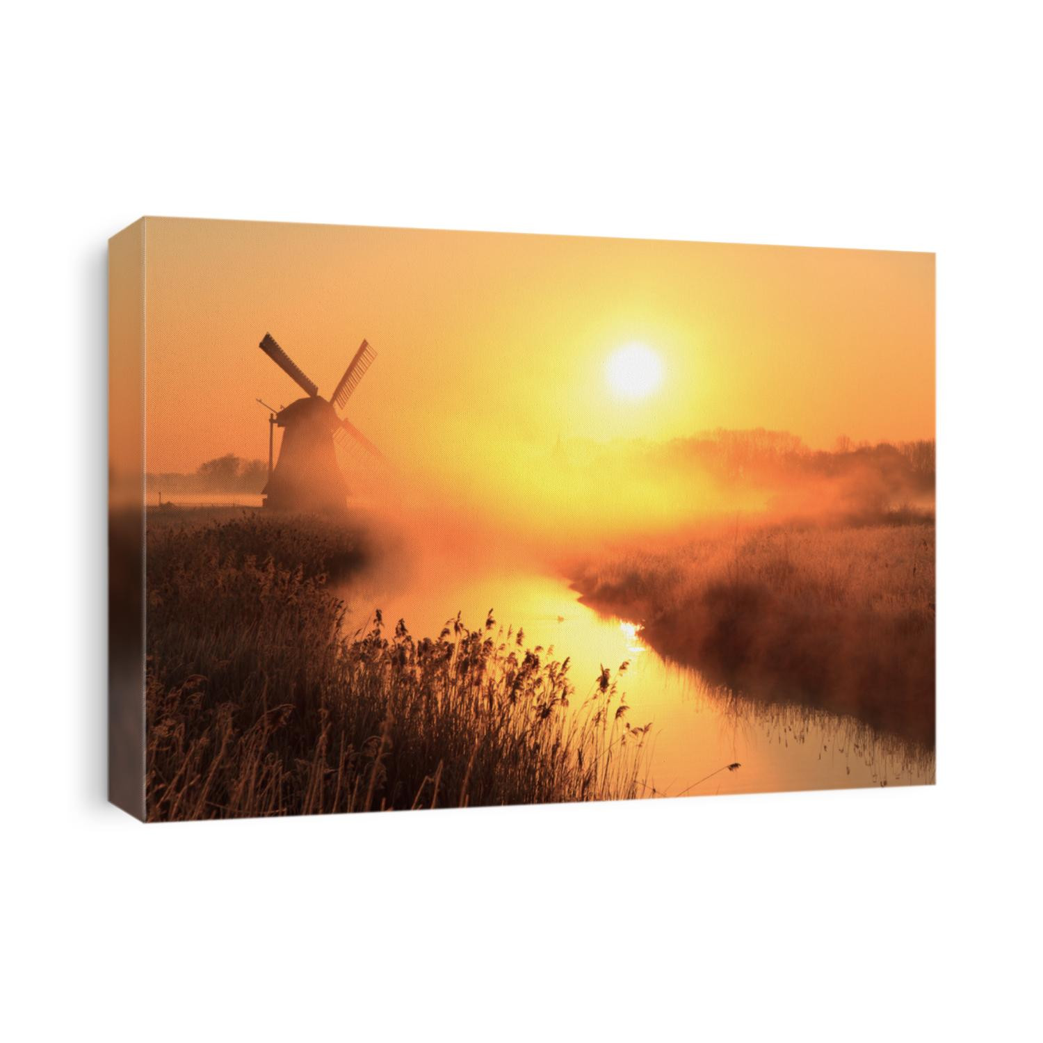 Dutch sunrise with traditional windmill and a canal in the spring fog.